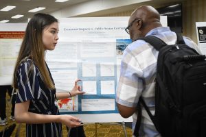 A student is presenting her poster presentation to another student at a conference