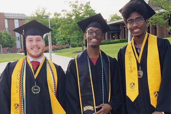 Three smiling undergraduate students in their cap and gown after their graduation